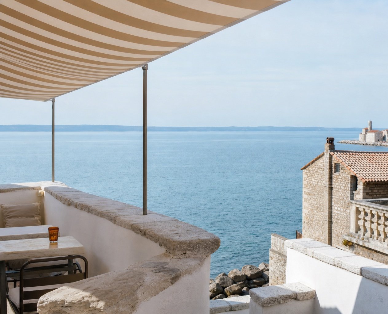 A sunlit Adriatic terrace overlooking the water and old stone houses of Piran